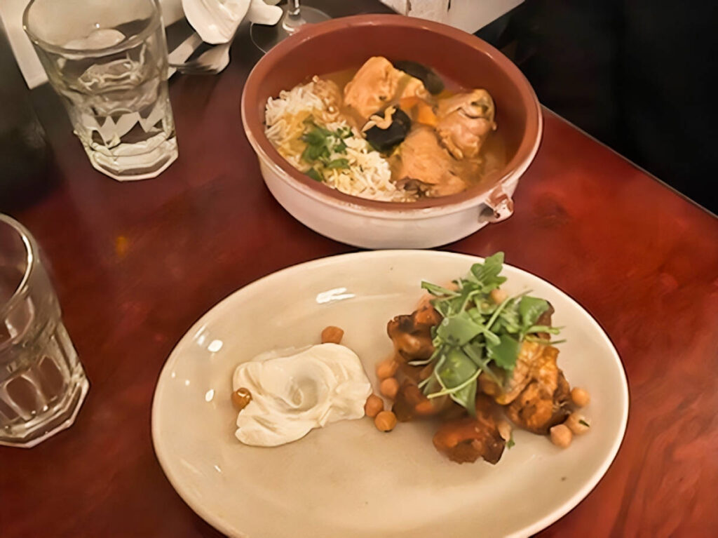 A bowl of chicken tagine and honey-glazed wings w/ a plate of chickpeas and a side of labneh from Cafe Mogador