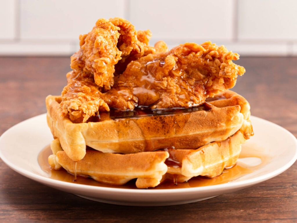 A plate of waffles, chicken and syrup on a wooden counter