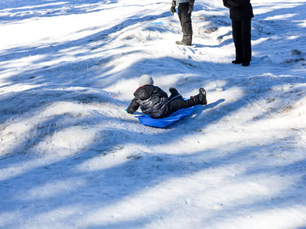 A young child sledding at the bottom of the hill in winter