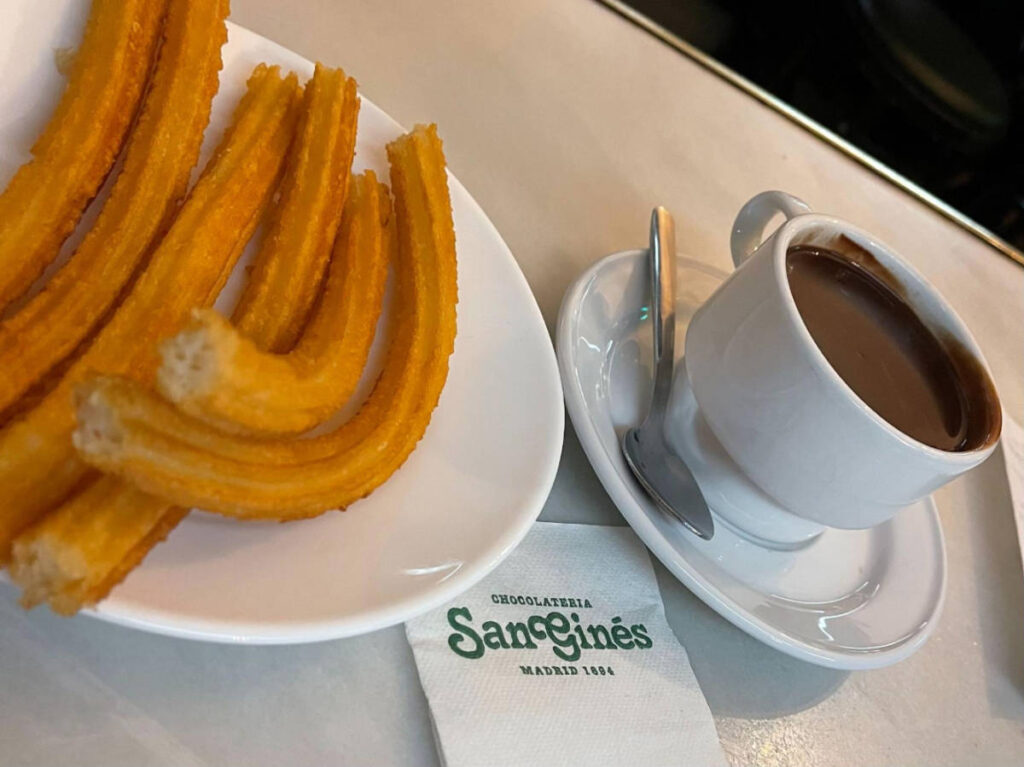 Churros on a plate and a cup of hot dark chocolate from Chocolateria San Gines