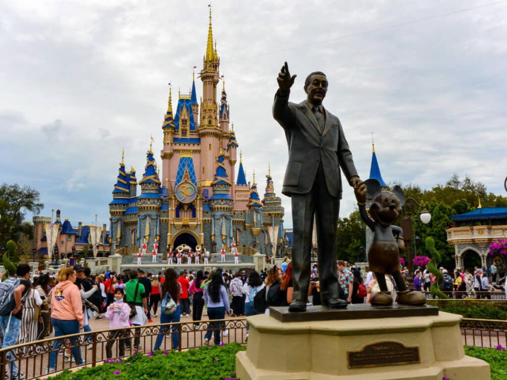 A statue of Walt Disney and Mickey Mouse in front of the Cinderella Castle