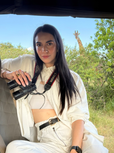 Travel Lemming writer Clara Kesseler, holding her binoculars with the giraffe peeking in the background