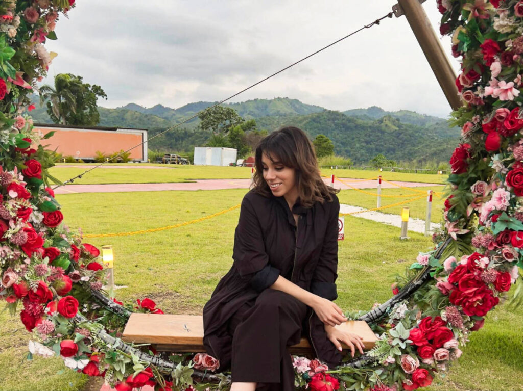 The author Claudicet Peña sitting on a chair surrounded by colorful flowers at the Jamaca de Dios Restaurante