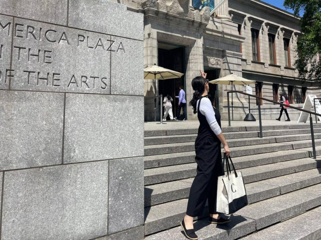 The author Claudicet Pena with a day bag in hand pointing the Museum of Fine Arts in the background