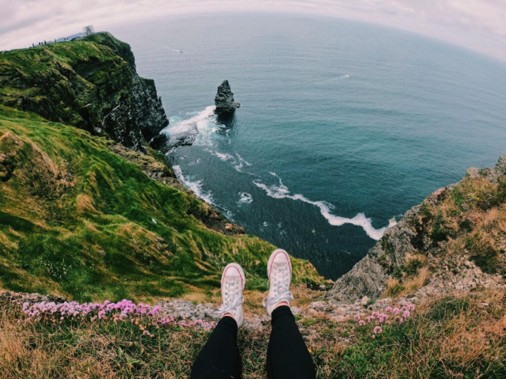 A person's feet on Cliffs of Moher in Ireland, overlooking the ocean