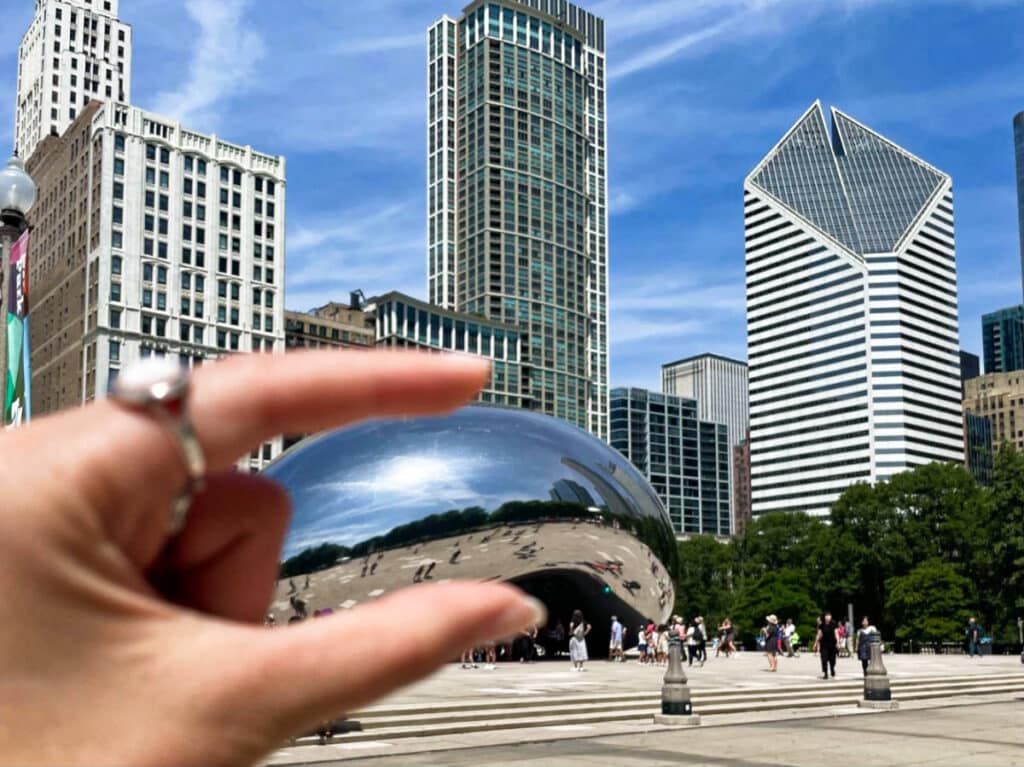 The iconic Cloud Gate landmark in between the fingers with the Chicago skyline in the background