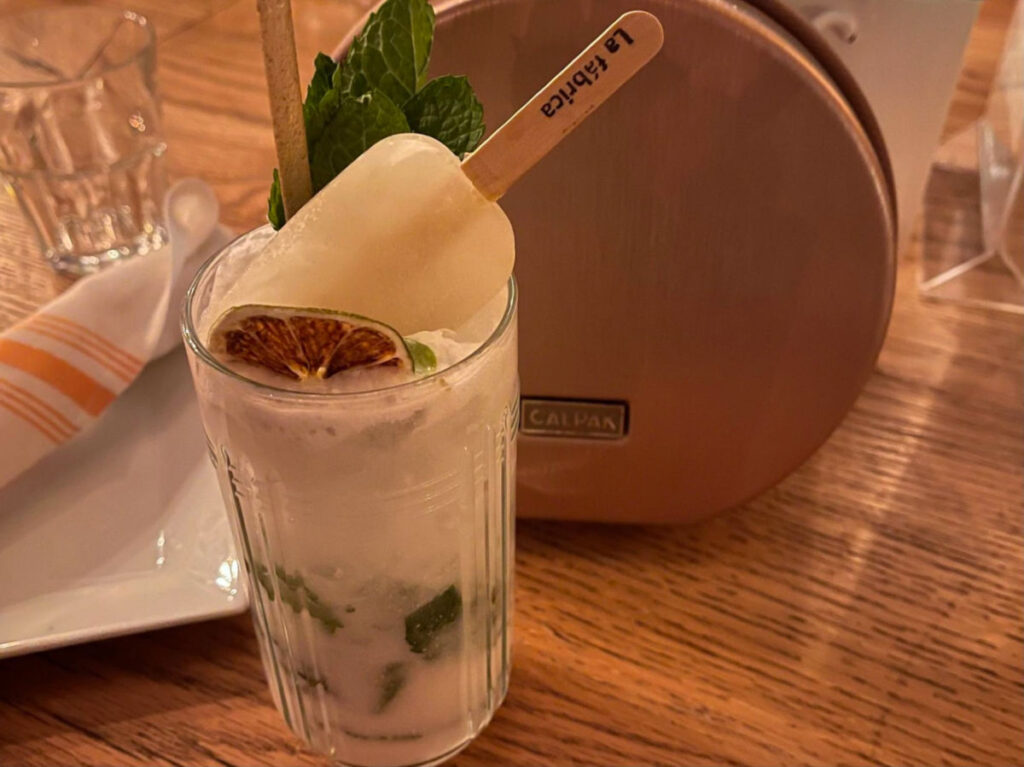 A Coconut Mojito with ice and fruit on a table at La Fabrica Central