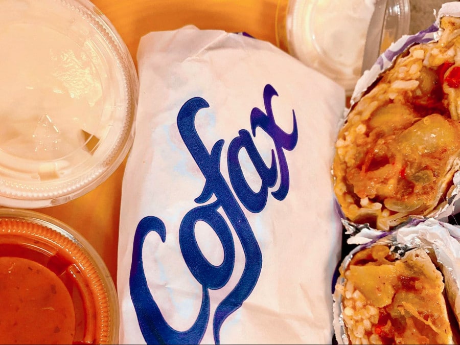 A packed and sliced in half burrito with two different sauces of Cofax