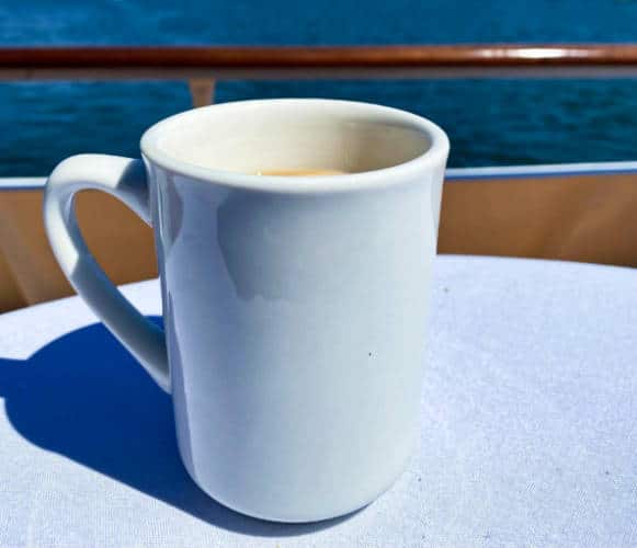 A white mug with coffee on the table near the ocean