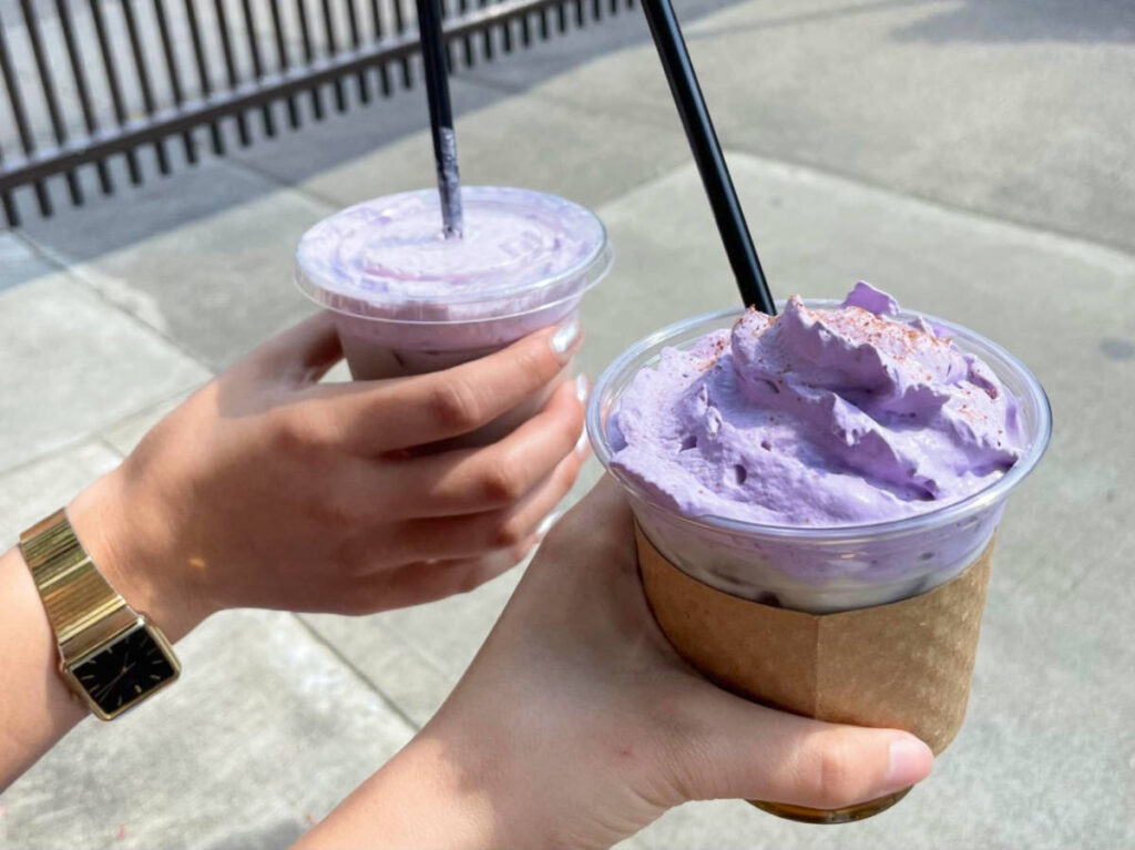 Two hands holding cups of coconut cold brew with ube whipped cream