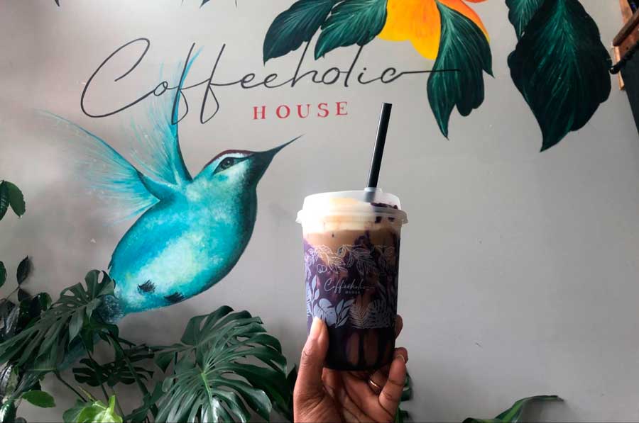 The author holding her drink with an art wall from Coffeeholic House on the background