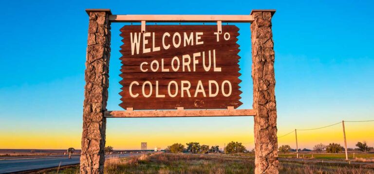 A "Welcome to Colorful Colorado" street sign with a colorful sky on the background