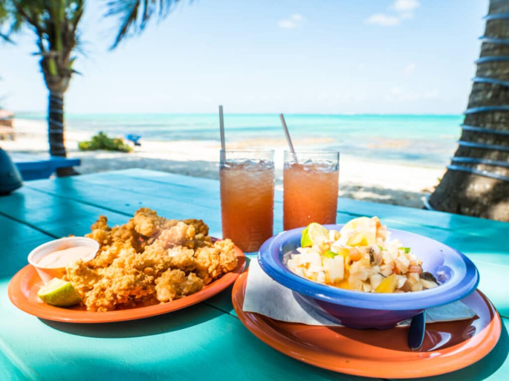 A plate of conch fritters, conch salad with punch on a table in the beach