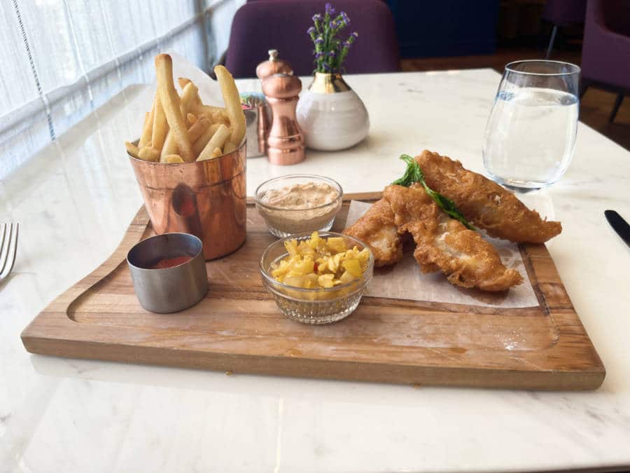 A serving of battered fish and fries with dips on a wooden board