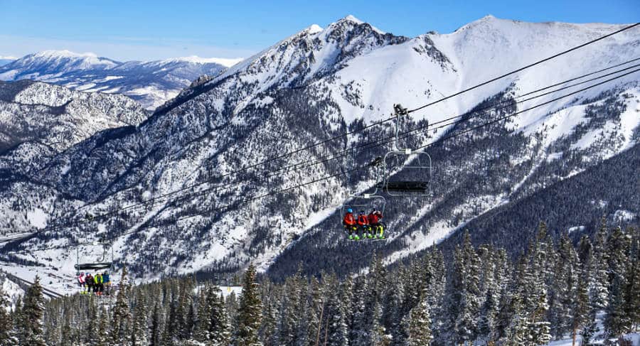 Skiers riding a chairlift with the background of snowcapped Colorado Rocky Mountains