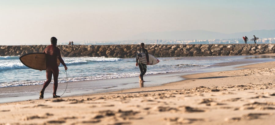 Surfers walking along the beach of Costa da Caparica with their surfboards
