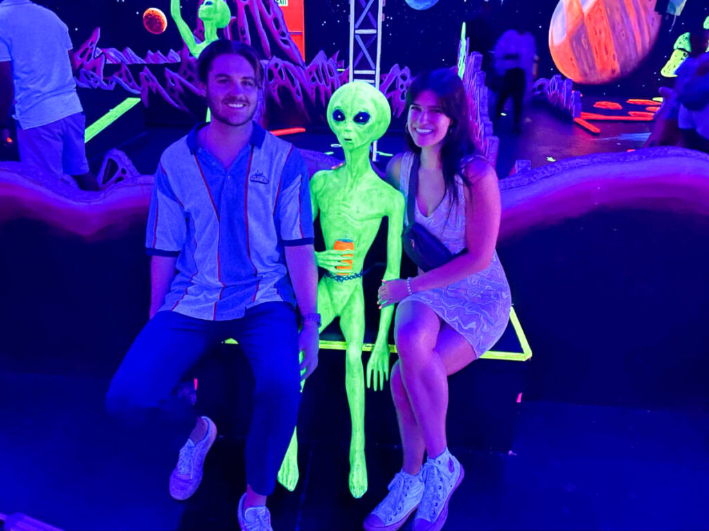 The author Betty Hurd and her boyfriend, posing for a photo with the illuminated neon alien figure inside the Imagine 3D Mini Golf