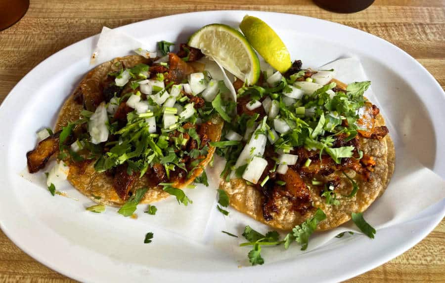 A serving of Tacos al pastor with sliced lemon on the plate at Coyotes Restaurant