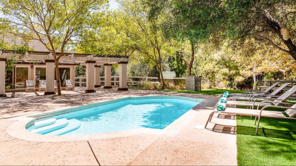View of the patio area with lounge chairs, lush green trees and a swimming pool