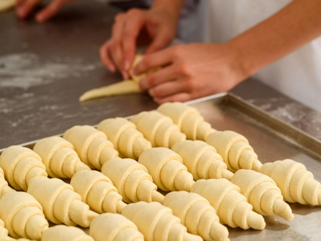 A person rolling dough into rolls to create classic croissants at the bakery shop