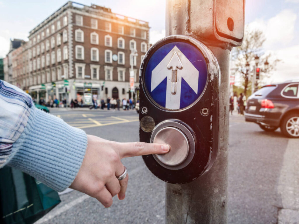 A woman's hand pressing a button to cross the street in Ireland
