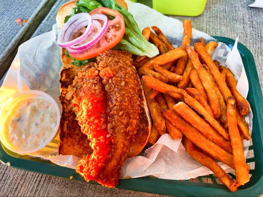 A crunchy fish sandwich with sauce, vegetables and fries from Squid Lips