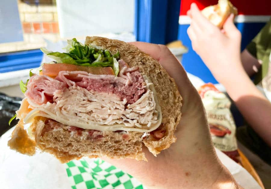 A hand holding the huge sandwich of D’Deli