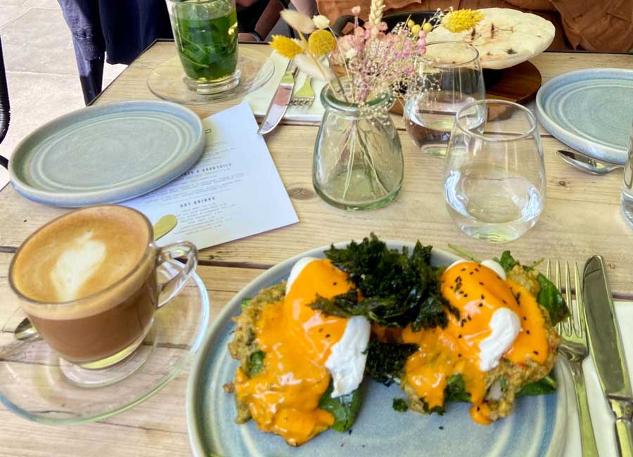 A cup of cappuccino and a eggs benny with Paprika Hollandaise on a plate in Delamina Marylebone