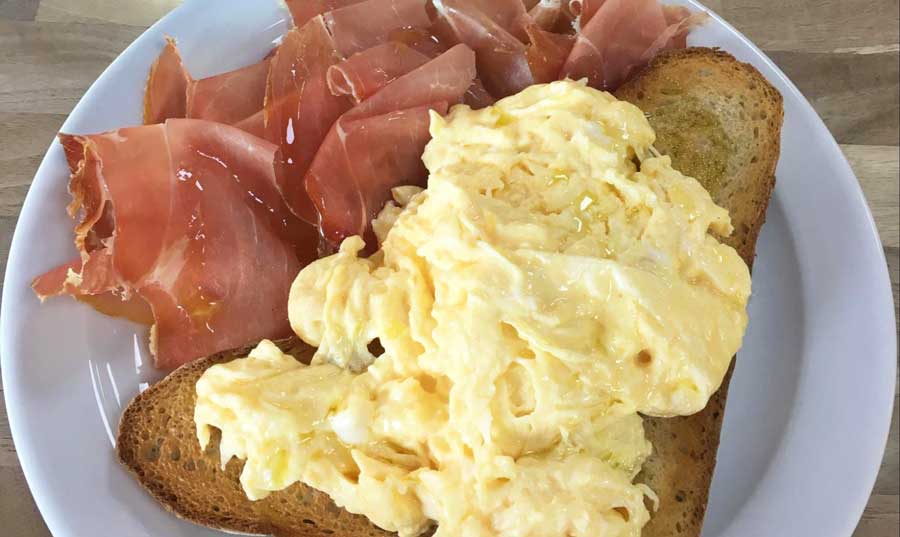 A toast wit fluffy egg and prosciutto on a plate in Delizie D’Italia
