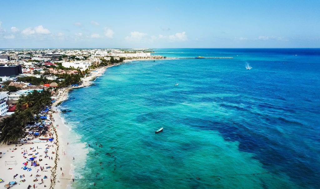 An overhead drone photo of the water, beach, and town of Playa del Carmen