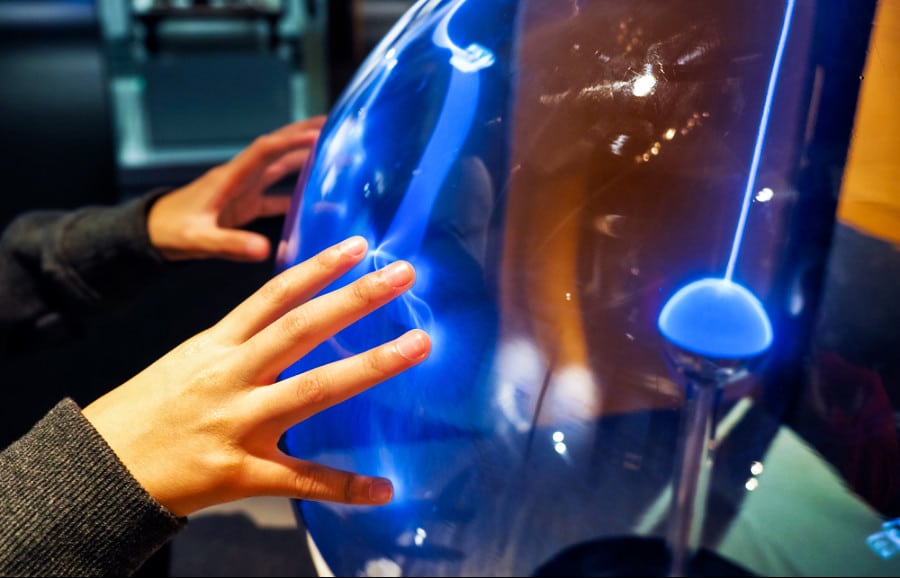 A closeup look of a hand of a child touching a plasma ball