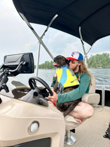 The author Abigail Bliss's husband, hugging their dog with a life vest while driving the boat