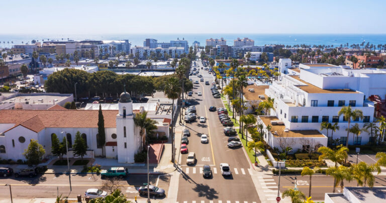 Aerial view of a bustling city street filled with cars and lined with tall buildings under a clear blue sky