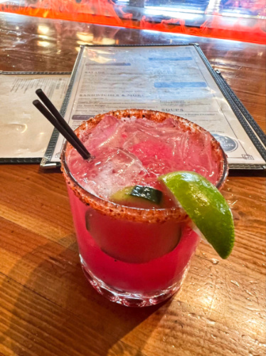 A glass of dragon fruit cocktail on the fake fire table in Belching Beaver Brewery Tavern and Grill