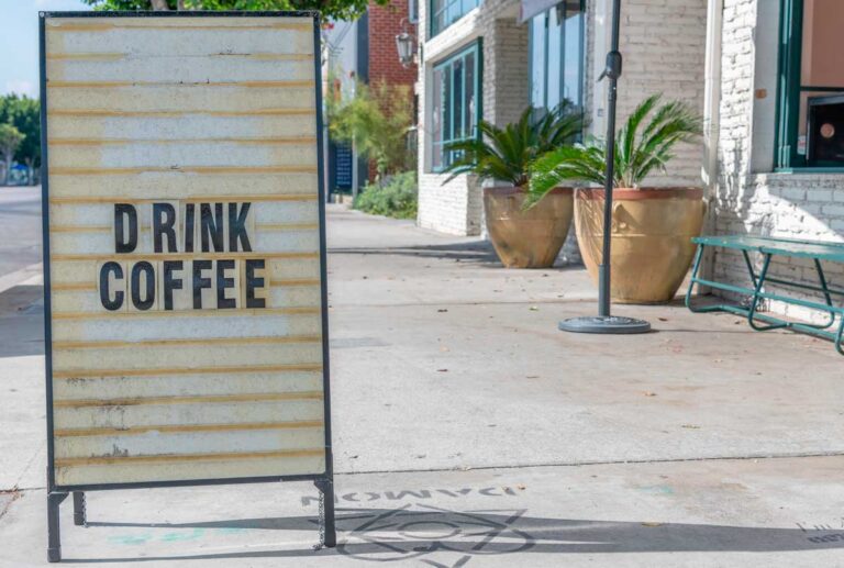 A drink coffee sign on a sidewalk