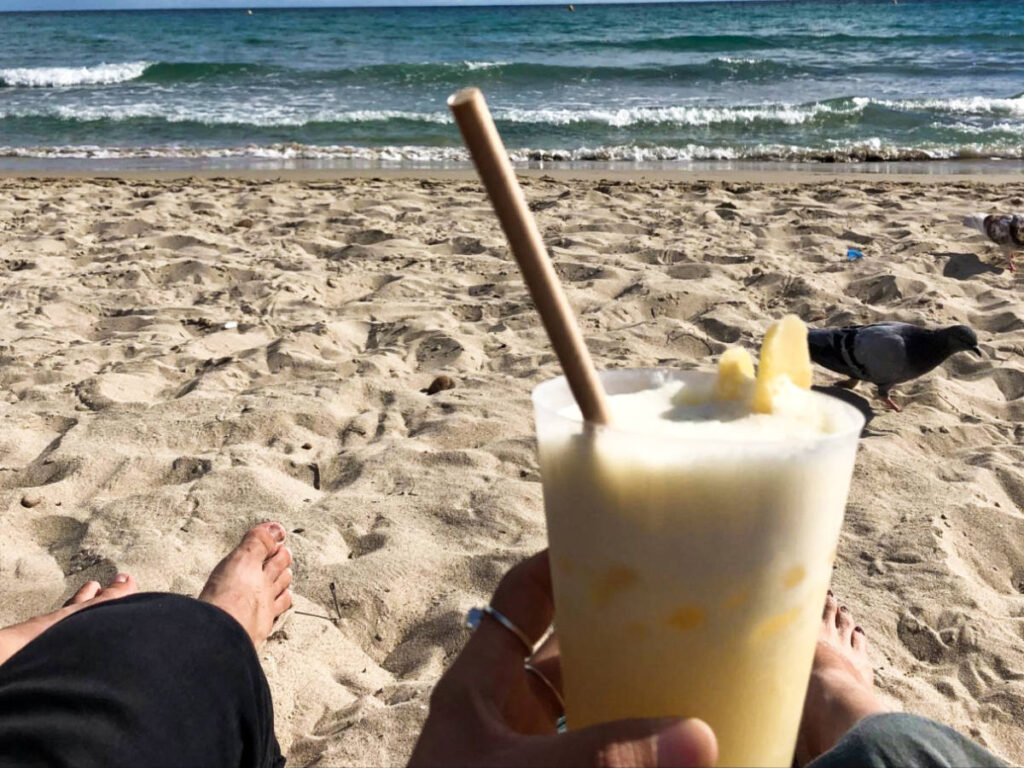 A hand holding a drink while chilling at the shoreline