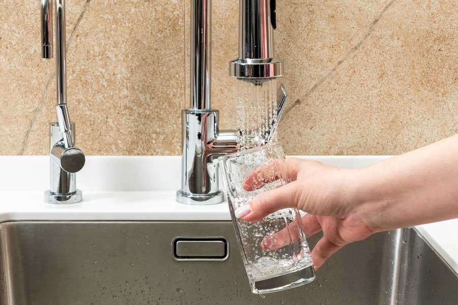 A woman's hand holding a glass getting a water on a faucet