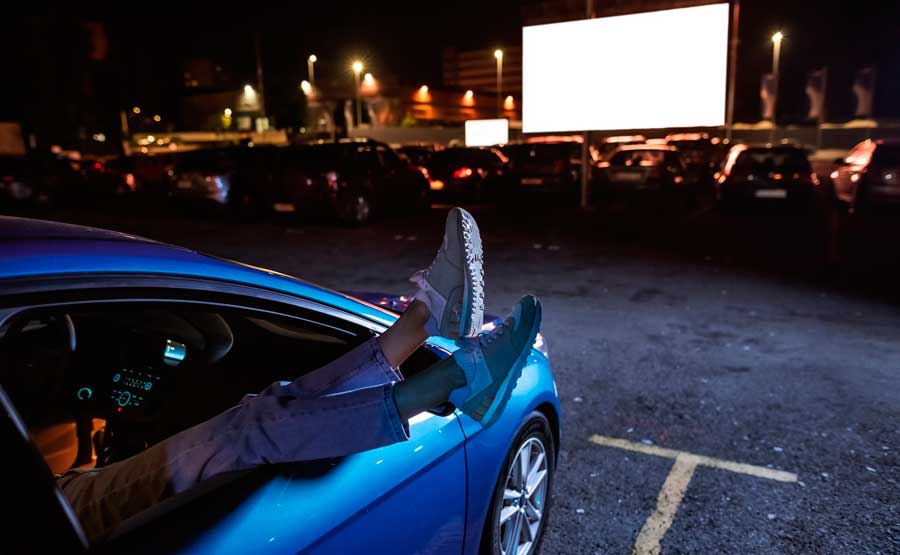 A woman hanging her legs out of the car window while on a drive-in movie