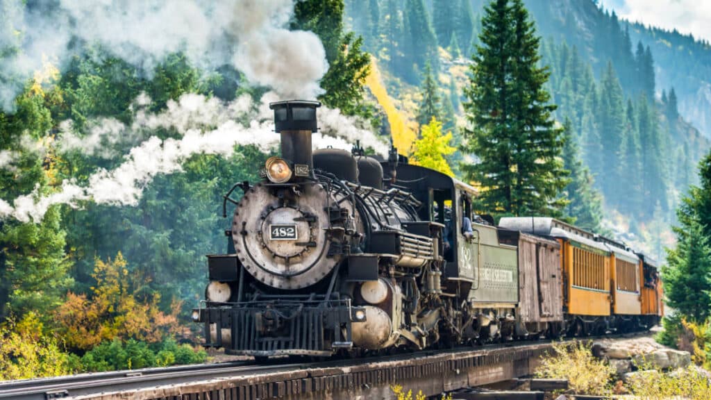 A steam train on the Durango & Silverton Railroad with a scenic view in the background during autumn