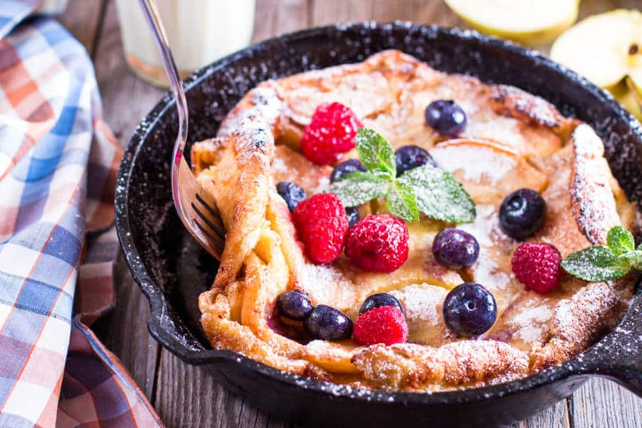 A pan of Dutch baby pancake with berries, apples and cinnamon