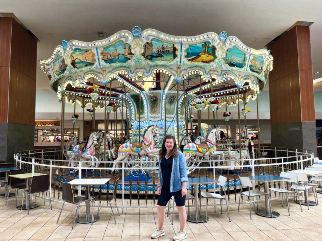 The author Elizabeth Demolat, wearing shorts and denim with a carousel in the background