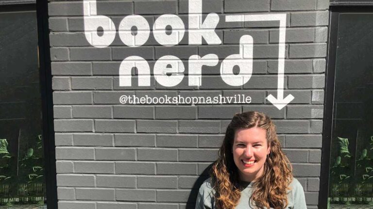 The author, Elizabeth Demolat, standing with the painted book nerd on a gray wall