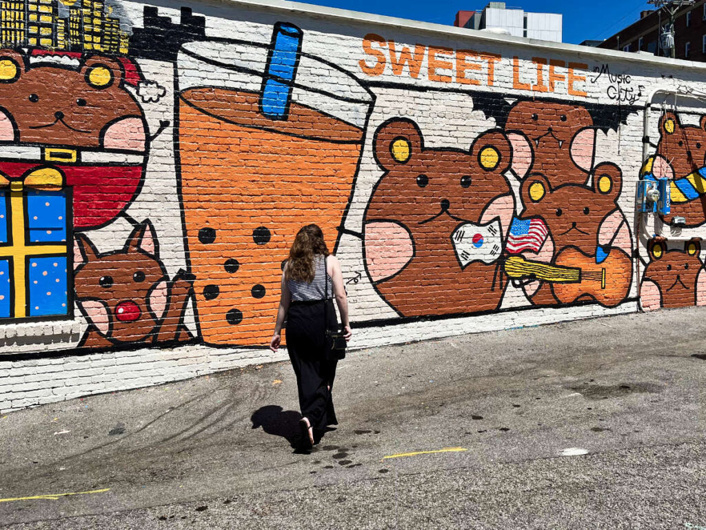 The author Elizabeth Demolat, walking to the mural wearing a tank top and skirt in the summer