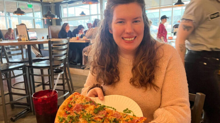 The author Elizabeth Demolat, holding a huge slice of pizza on a plate from Five Points Pizza