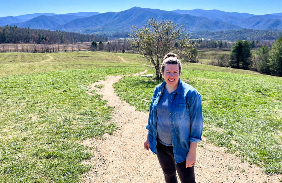 The author, Elizabeth, posing in the middle of the trail in Cades Cove Loop with a scenic mountain view in the background