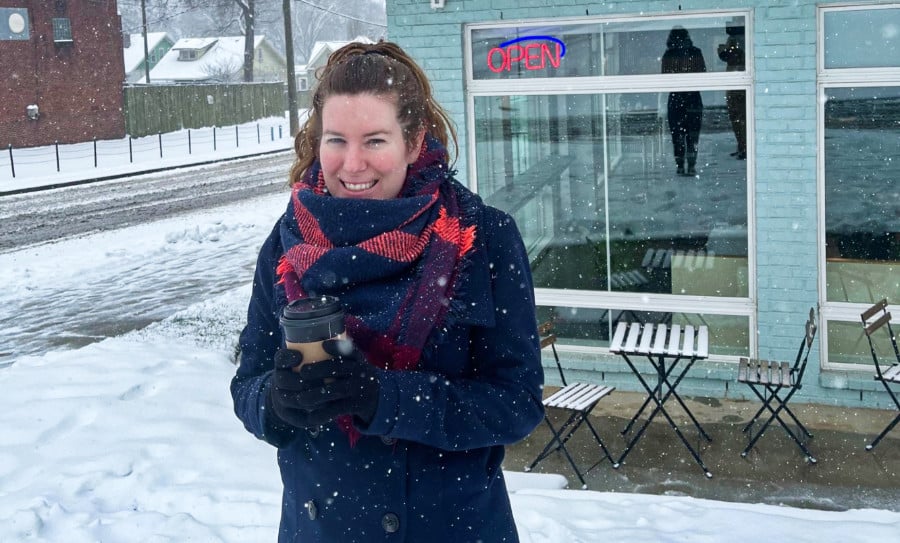 The author Elizabeth Demolat standing outside the snowy weather while holding a coffee cup