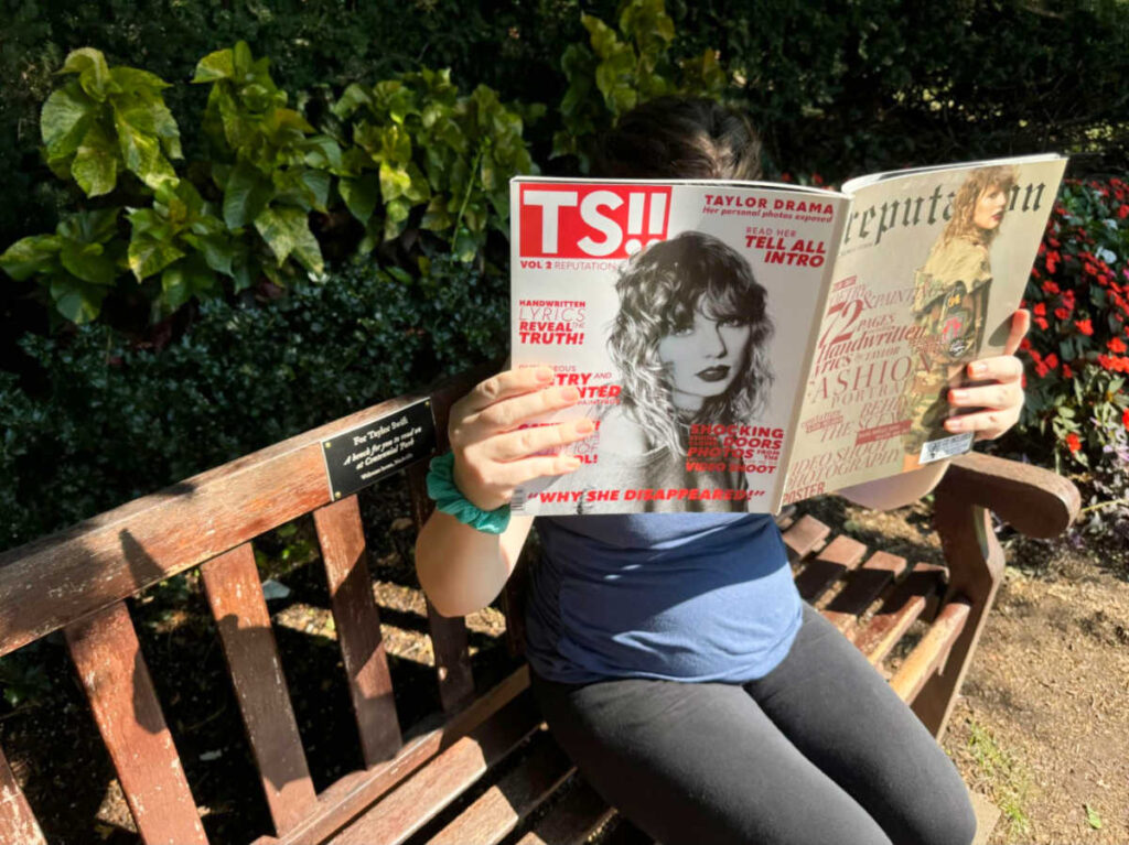 The author Elizabeth reading a Taylor Swift magazine on the Taylor Swift bench