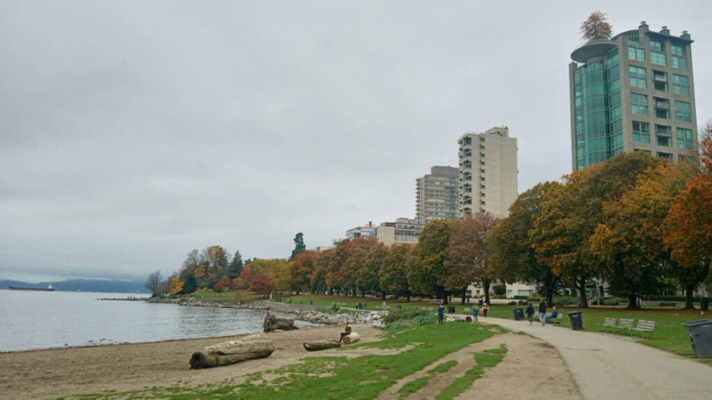 Panoramic view of the English Bay Beach surrounded by fall foliage with the highrises in the background