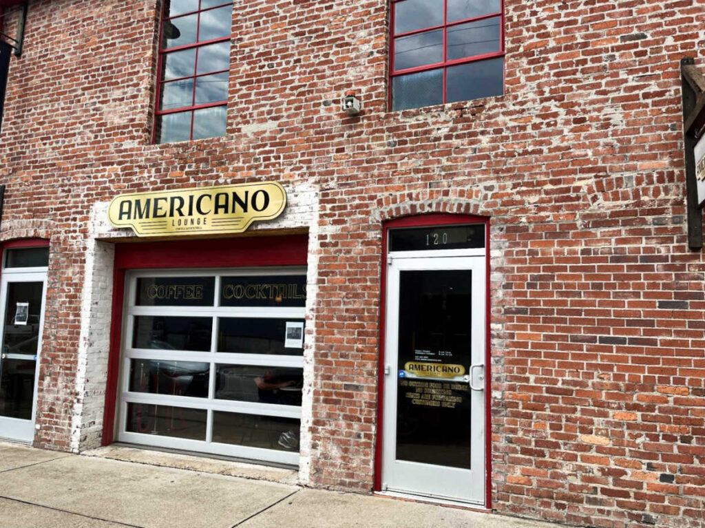 View of the brick walled exterior and white entrance door of Americano Lounge