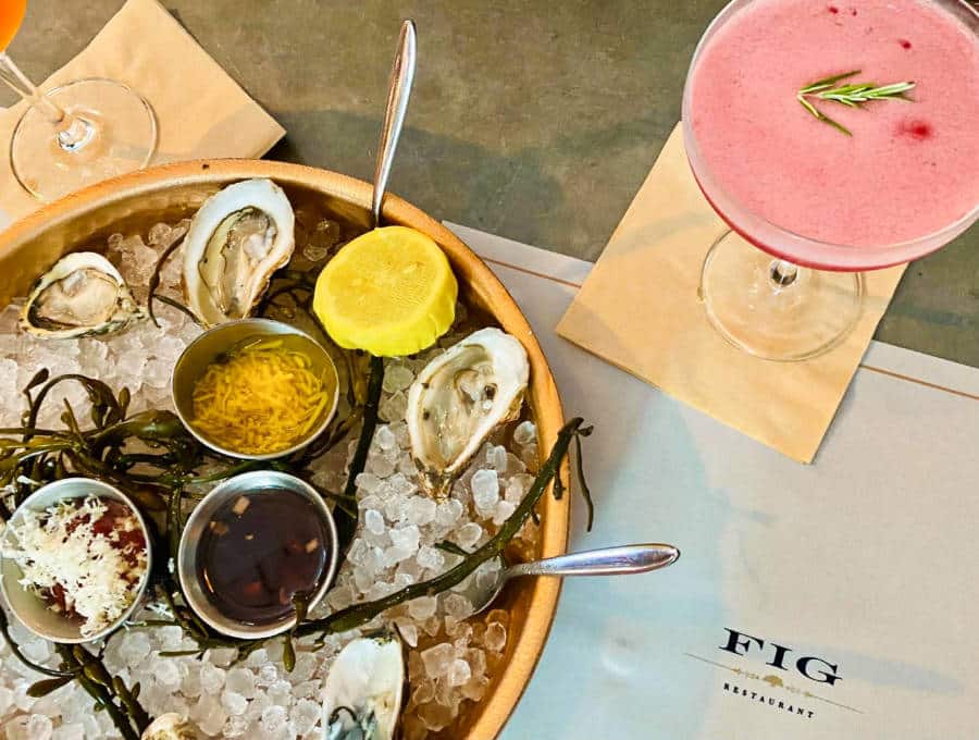 Fresh oysters with sliced lemon, sauce and toppings served on ice with a glass of cocktail on the side